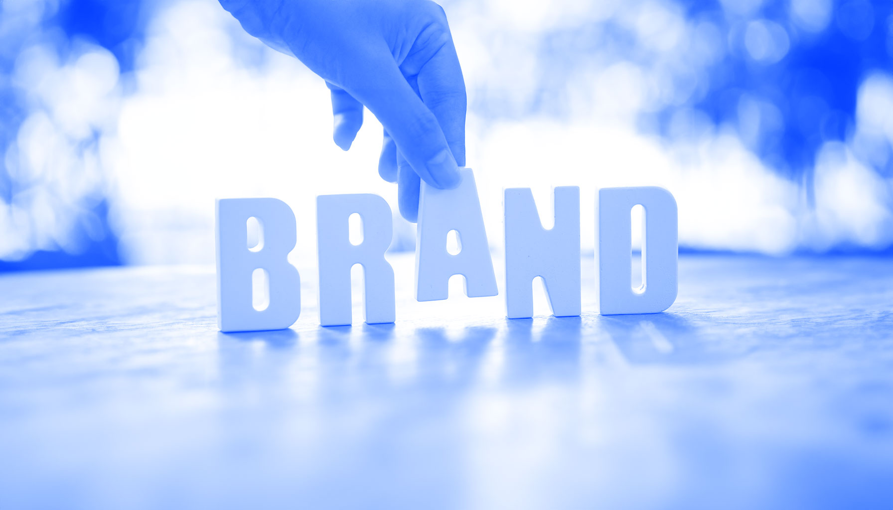 Hand arrangiert weiße Buchstaben zum Wort „BRAND“ auf Holzoberfläche mit verschwommenem Hintergrund